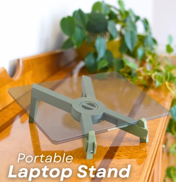 A portable laptop stand with a clear glass top, placed on a wooden surface next to a potted plant.