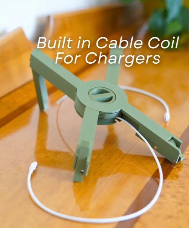 A green cable organizer designed to hold and organize cables for chargers, with a white cord visible on the table.
