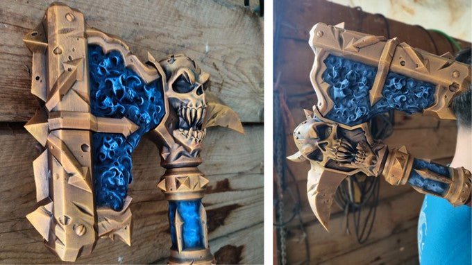 two detailed and intricately designed fantasy weapons, including a large sword and a large hammer, both adorned with a skull and crossbones motif. The weapons are displayed against a wooden background, showcasing their craftsmanship and the artistic style of the creator.