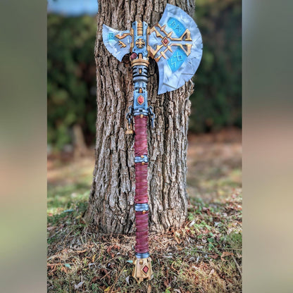 A large, ornate, and intricately designed sword is leaning against a tree trunk in a natural outdoor setting.