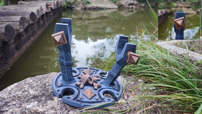a blue and brown metal sculpture situated on a rock near a body of water, with a wooden bridge visible in the background.
