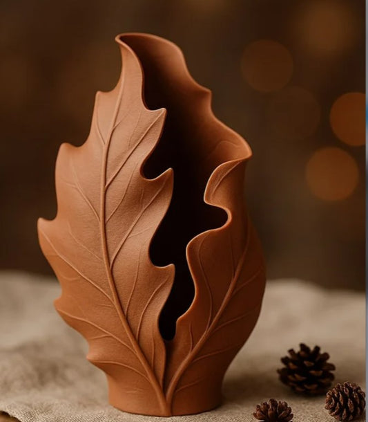 A ceramic vase with a leaf-like design sits on a surface, surrounded by pine cones.