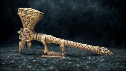 A golden, intricately designed sword or weapon with a pointed end and a cross-like symbol on the side, displayed on a stand against a dark background.