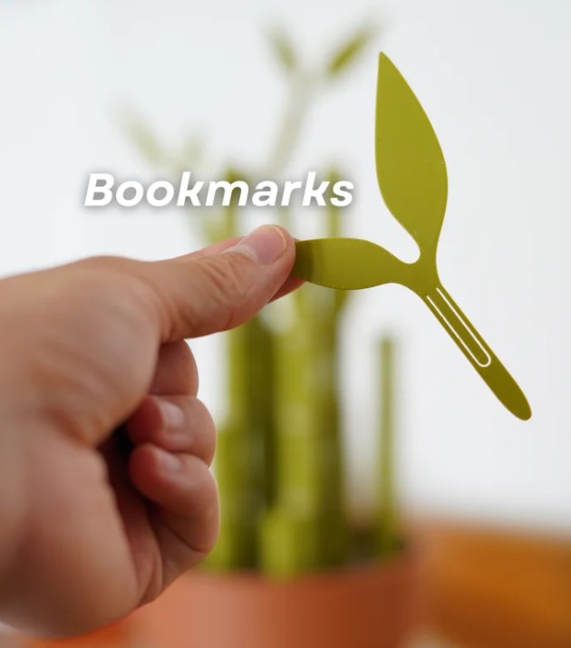 A hand holding a green bookmark shaped like a plant or leaf, with the word "Bookmarks" written on it.
