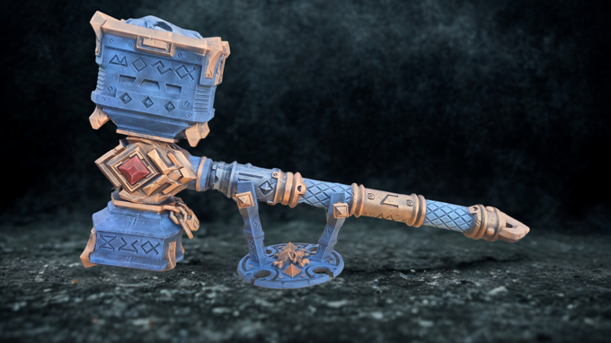 A blue and gold hammer with intricate designs and patterns, displayed on a dark surface.