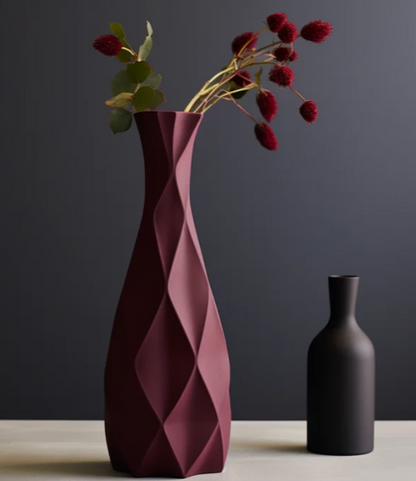 a tall, red vase with a geometric pattern and a bouquet of red flowers in it, placed next to a smaller black vase on a dark surface.