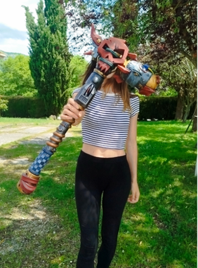 A person is standing in a grassy area, holding a large, colorful object that resembles a weapon or tool.