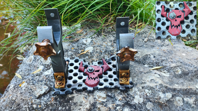 a collection of metal objects, including a metal frame with two handles and a metal plate with a skull design, all set against a natural background.