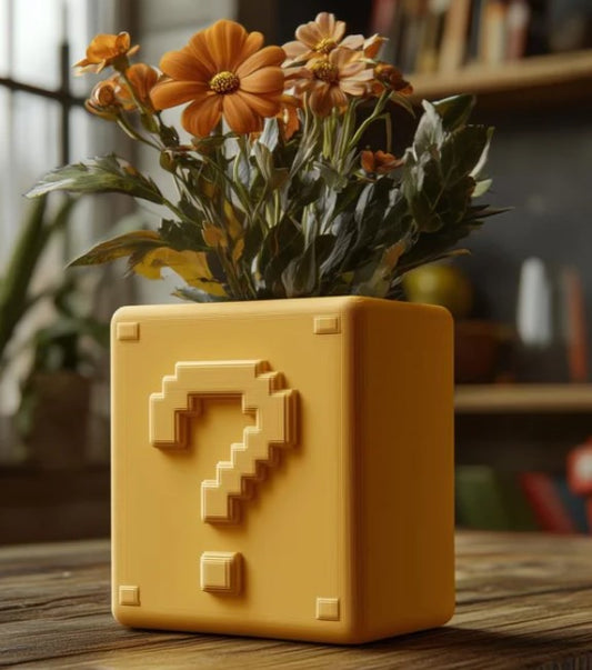 A yellow vase with a pixelated question mark design, filled with orange flowers, sits on a wooden surface.