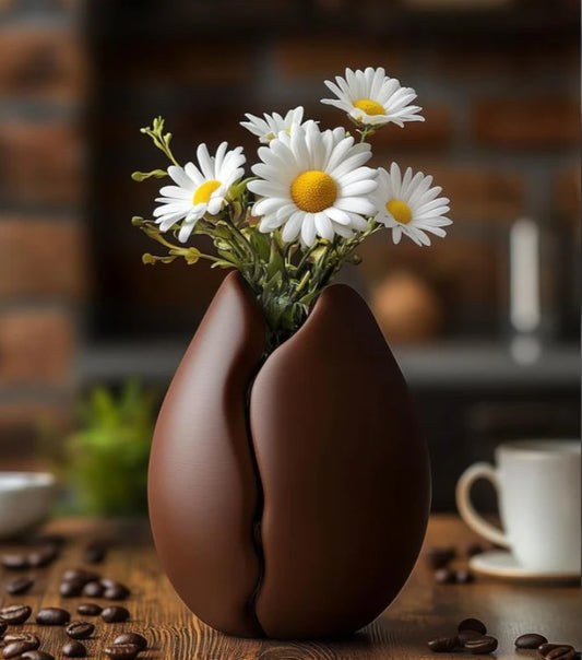 A vase filled with white daisies sits on a wooden surface, with coffee beans scattered around it.